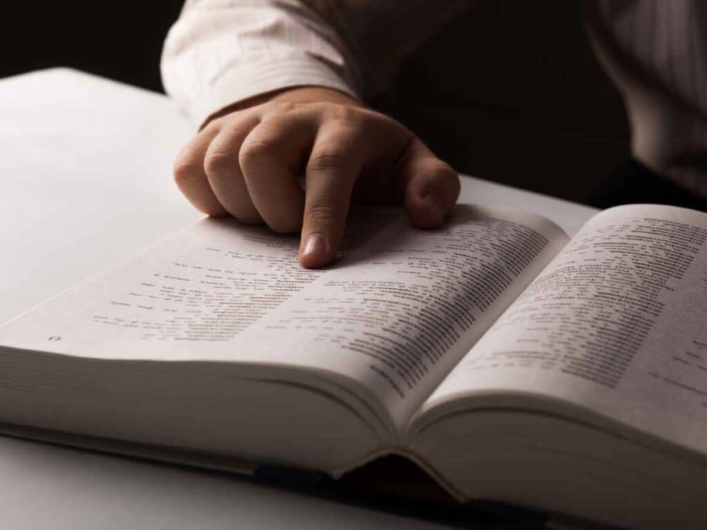 Pessoa lendo o novo acordo ortográfico, pesquisando no livro informações sobre "caju" ou "cajú".